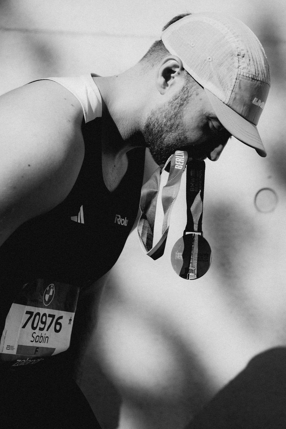 Berlin Marathon finisher wearing a LUMEN cap with a medal, photographed in black and white